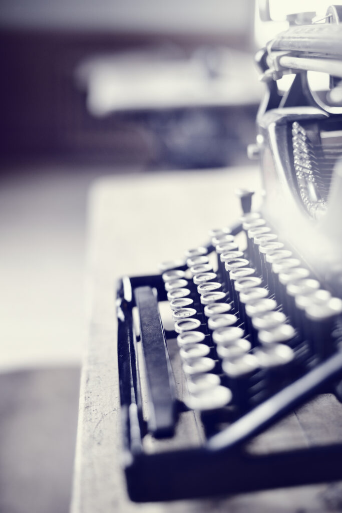 Side view of an old-fashioned black metal typewriter on a wooden desk. Toned image.